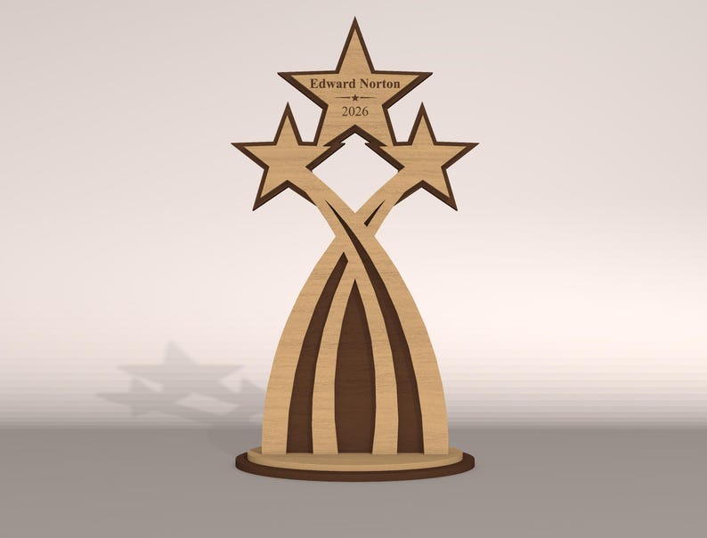 May include: A wooden trophy featuring three stars and the name "Edward Norton" with the year "2026" engraved on the top star. The design incorporates curved lines and a circular base, with a two-tone brown color scheme.