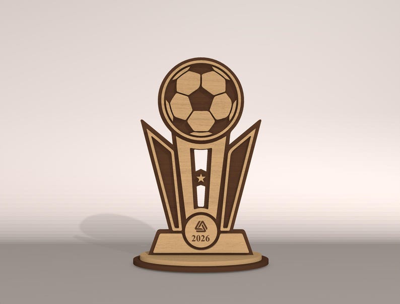 May include: Wooden soccer trophy with a soccer ball at the top. The trophy has a light brown base and a dark brown accent. The year 2026 is printed on the base. The trophy is designed with geometric shapes.