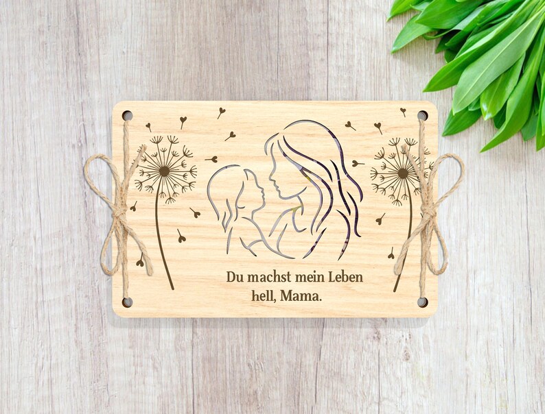 May include: Wooden sign with a cutout design of a mother and child, with dandelion accents. The text reads "Du machst mein Leben hell, Mama."