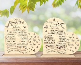 Può includere: Due targhe di legno a forma di cuore con messaggi incisi per una moglie. La targa a sinistra recita "To My Beautiful Wife" e la targa a destra recita "To My Wife". Entrambe le targhe mostrano una coppia che si tiene per mano e farfalle.