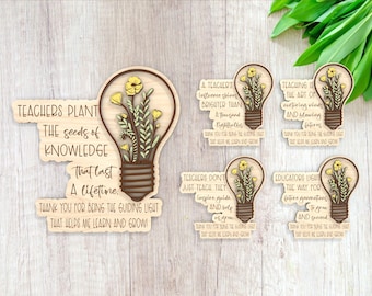 May include: Set of six wooden lightbulb-shaped ornaments with inspirational messages for teachers. Each ornament features a yellow flower design and the text "Teachers plant the seeds of knowledge that last a lifetime."  "A teacher's influence shines brighter than a thousand lightbulbs." "Teaching is the art of nurturing minds and blooming futures." "Teachers don't just teach, they inspire, guide, and help us grow." "Educators light the way for future generations to grow and succeed."
