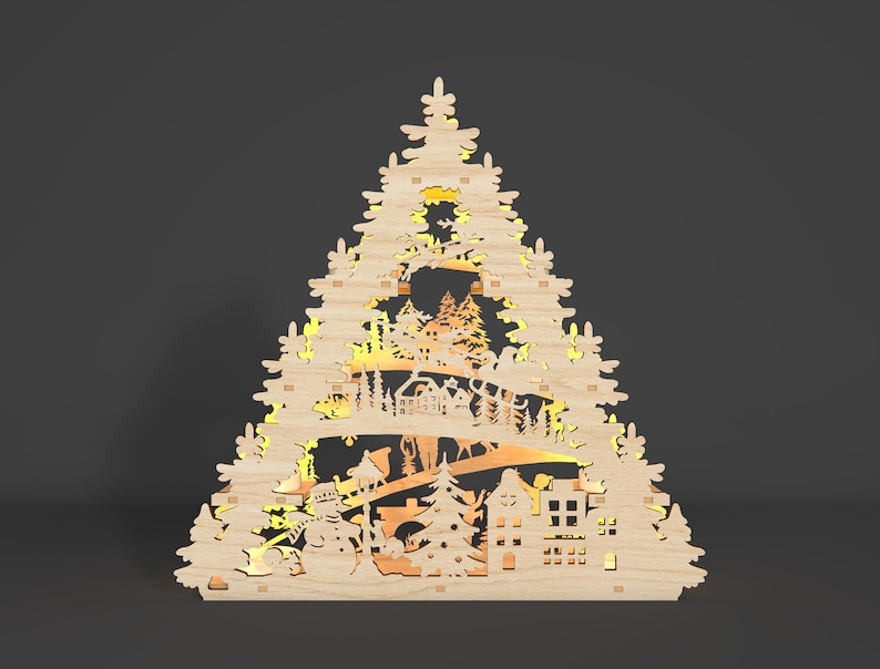 May include: A wooden Christmas tree decoration featuring a cut-out design of a winter village scene. The decoration is illuminated from behind, creating a warm glow. The scene includes houses, trees, a snowman, and a deer.