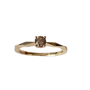 Puede incluir: Un anillo de oro con una sola piedra preciosa redonda de color marr&oacute;n claro engastada en el centro.