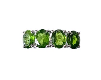 May include: A silver ring featuring four oval-cut, vibrant green gemstones. The gemstones are set in a row, creating a continuous band of color. The ring's design is simple, highlighting the brilliance of the green stones.