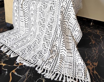 May include: Black and white throw blanket with a geometric pattern and fringe. The blanket is draped over a chair.