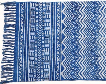May include: A blue and white cotton rug with a geometric pattern. The rug has a fringe on one side.