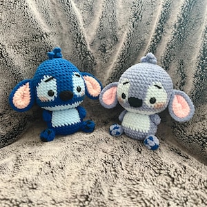 May include: Two crocheted Stitch plush toys. One is blue with light blue accents and the other is gray with white accents. Both have pink ears and black eyes.