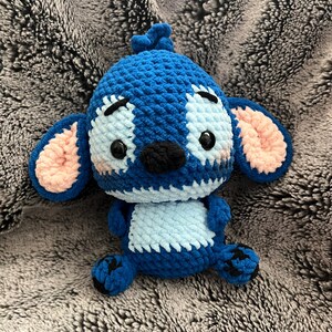 May include: A blue and light blue crocheted Stitch plush toy with pink ears and black eyes.