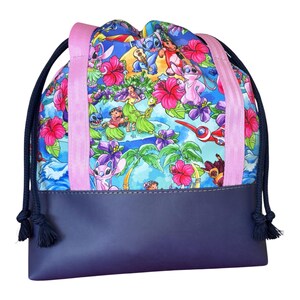 May include: A drawstring backpack featuring a vibrant blue fabric printed with cartoon characters, pink hibiscus flowers, and palm trees. The bag has a solid dark navy blue base, two light pink vertical straps, and dark navy blue rope drawstrings.