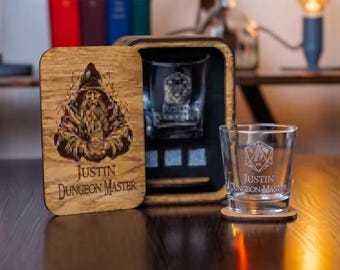 May include: A wooden box with a sliding lid featuring a colorful wizard illustration and the text "Justin Dungeon Master," containing a clear glass tumbler. A matching glass tumbler with the same text and a 20-sided die icon sits on a wooden coaster.