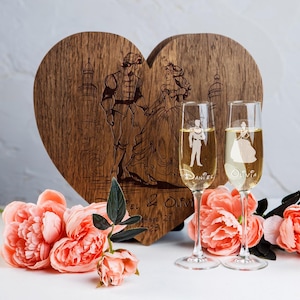 Può includere: Due flute da champagne con silhouette incise di un principe e una principessa, con i nomi "Daniel" e "Olivia" sotto. Le flute sono davanti a una scatola di legno a forma di cuore con un'immagine incisa di un principe e una principessa.