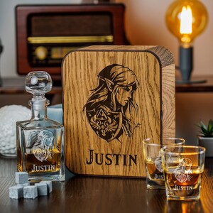 May include: A wooden box with a personalized inscription "Justin" and a graphic of a character from a video game. The box includes two engraved glasses and a decanter with a matching design.