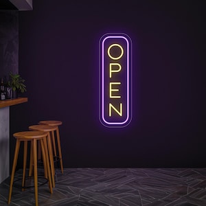 May include: A vertical neon sign with the word "OPEN" in yellow letters, outlined in a purple border, is mounted on a dark purple wall. The sign is illuminated, suggesting a business is open. Wooden stools and a bar are in the background.