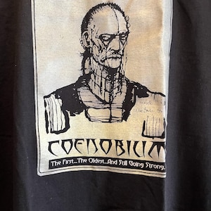 May include: Black and white graphic t-shirt with a drawing of a man's face and the text "COENOBIUM The First...The Oldest...And Still Going Strong."