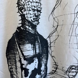 May include: Black and white illustration of a character with a grid-like head and a dark, textured outfit. The character is standing with their arms crossed and has a serious expression.