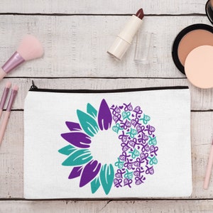 May include: White zippered makeup bag with a purple and teal sunflower design. The sunflower is made up of multiple purple and teal ribbon shapes.