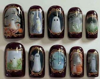 May include: Set of ten burgundy-colored press-on nails, each featuring a unique hand-painted Halloween ghost design. The ghosts are depicted in various scenes, framed with gold accents, creating a spooky and artistic aesthetic.