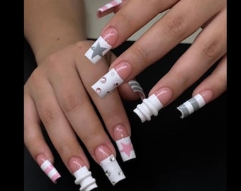 May include: A set of long, square-shaped acrylic nails. The nails feature various designs, including white with gray stars, pink stars, clear rhinestones, and white and gray stripes. Some nails have a 3D textured design.