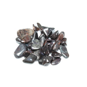 May include: A pile of black and red hematite tumbled stones. The stones are smooth and polished, with a metallic sheen.