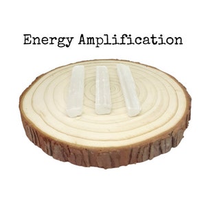 May include: Three white selenite sticks on a wooden slice. The sticks are arranged in a row and are about 3 inches long. The text "Energy Amplification" is written above the sticks.