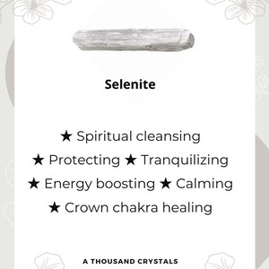 May include: A white selenite crystal, a type of mineral known for its calming and cleansing properties. The text on the card reads "Selenite", "Spiritual cleansing", "Protecting", "Tranquilizing", "Energy boosting", "Calming", "Crown chakra healing", and "A Thousand Crystals".