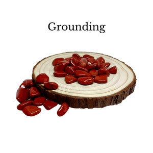 Könnte beinhalten: Rote Erdungssteine auf einer Holzscheibe. Die Steine sind geschliffen und glatt. Der Text "Grounding" steht über den Steinen.