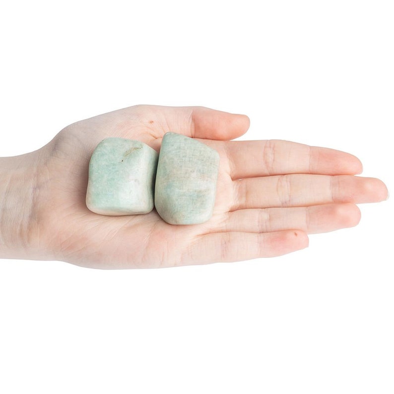 May include: Two smooth, light green, tumbled stones in a hand. The stones are a pale green color and have a smooth, polished surface.