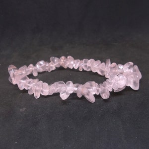 May include: A pink rose quartz chip bracelet. The bracelet is made of small, irregular pieces of rose quartz that are strung together on a clear elastic cord.