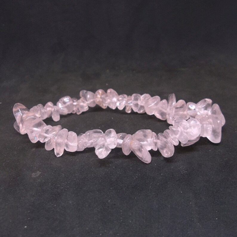 May include: A pink rose quartz chip bracelet. The bracelet is made of small, irregular pieces of rose quartz that are strung together on a clear elastic cord.
