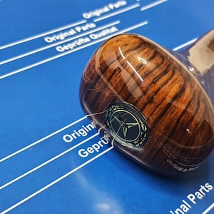 以下が含まれることがあります： 銀色のトリムと黒と銀のロゴが付いた木製のシフトノブ。ノブは濃い茶色の木目模様です。