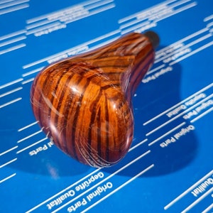 Op de afbeelding: Een bruine houten versnellingspookknop met een donkerbruin en lichtbruin houtnerfpatroon.