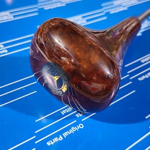 May include: A brown wooden gear shift knob with a blue and gold emblem. The knob is on a blue surface with white lines.