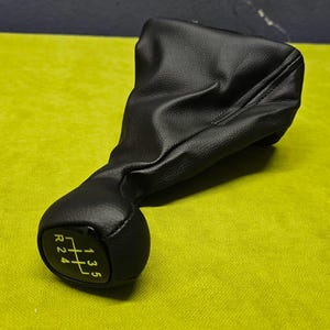 May include: Black leather gear shift knob with a black plastic base and yellow numbers for the gears: R, 1, 2, 3, 4, 5.
