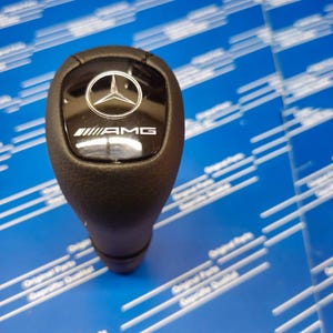 May include: Black leather gear shift knob with a silver AMG logo and a black Mercedes-Benz logo.