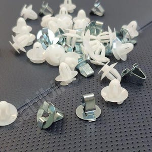 Puede incluir: Primer plano de un montón de sujetadores de plástico blanco con clips metálicos. Los sujetadores se utilizan para sujetar los paneles interiores del automóvil.