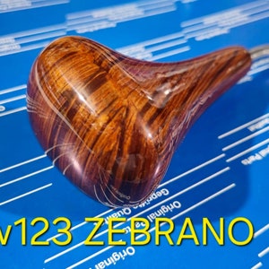 以下が含まれることがあります： ゼブラウッド模様の木製シフトノブとクロム色の金属シャフト。ノブは濃い茶色で、薄い茶色と白の縞模様があります。「w123 ZEBRAÑO」の文字は黄色です。