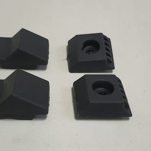 May include: Four black plastic pieces with different shapes and designs. Two pieces have a flat top and a rounded bottom, while the other two have a flat top with a hole and a series of ridges on the side.