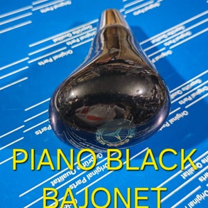 Pode incluir: Uma alavanca de câmbio preta com uma moldura prateada e um logotipo da Mercedes-Benz. A alavanca é etiquetada como "PIANO BLACK BAJONET".