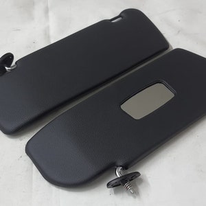 Puede incluir: Dos viseras para el sol de coche negras, una de ellas con un pequeño espejo.