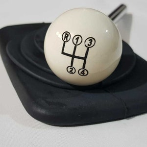 May include: White ball gear shift knob with black printed numbers and letter 'R' for reverse, 1, 2, 3, 4, and a black gear shift pattern.