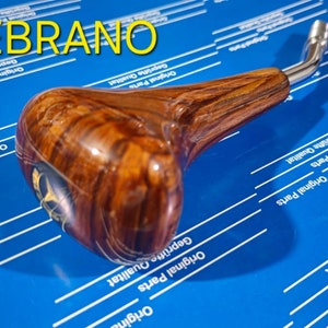 Peut inclure: Un pommeau de levier de vitesse en bois avec un levier argenté. Le pommeau a un motif de grain de bois brun et noir. Le texte "W124 ZEBRANO" est visible dans le coin supérieur gauche de l'image.