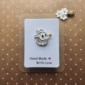 May include: A white enamel pin depicting a cartoon dog with a red collar and orange nose. The pin is on a white card with the text "Hand Made With Love". The background is a brown card with white polka dots.