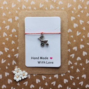 May include: A white card with red string and a silver baby carriage charm. The card says "Hand Made with Love".