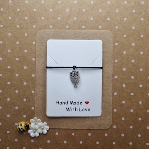 Può includere: Un braccialetto di corda nero con un ciondolo a forma di gufo argentato. La carta attaccata al braccialetto recita "Hand Made With Love".