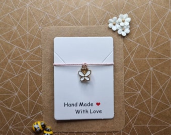 May include: A white card with pink string and a gold butterfly charm. The card says "Hand Made with Love" and has a red heart.