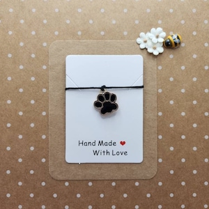 May include: A white card with black text that reads "Hand Made With Love" and a red heart. A black paw print charm hangs from a black string.