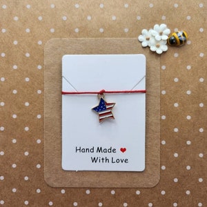 May include: A red string with a gold star charm featuring the American flag design. The card reads "Hand Made With Love".