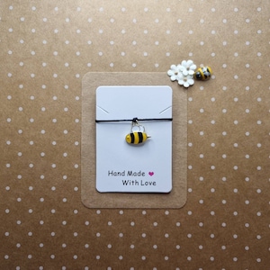 May include: A black string bracelet with a small gold bee charm. The card reads "Hand Made With Love".
