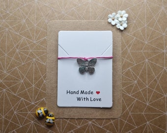 May include: A white card with a pink string tied around it. A silver butterfly charm hangs from the string. The card says "Hand Made with Love" and has a red heart symbol.