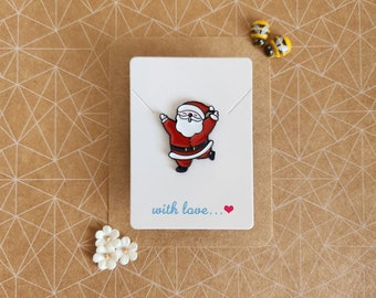 May include: A white card with a red and white cartoon Santa Claus enamel pin. The card has the text "with love..." written in blue with a red heart.
